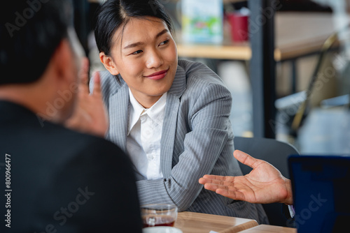 The image shows a young Asian businesswoman sitting at a table and talking to two colleagues. photo