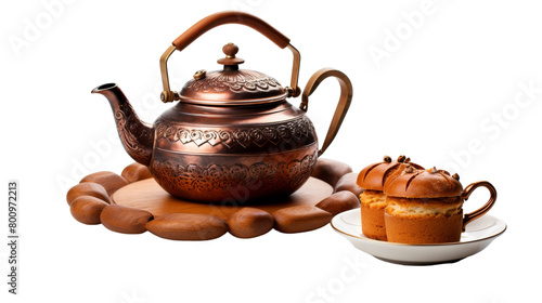 A delicate tea pot sits next to a plate holding a mouthwatering muffin