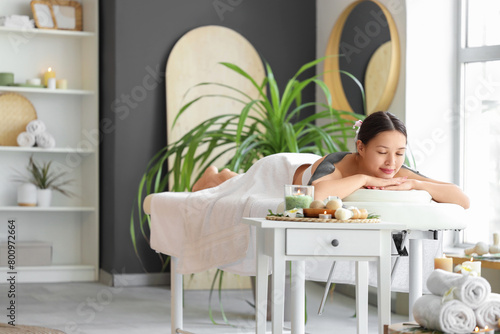 Beautiful Asian woman with mud on her shoulders lying in spa salon