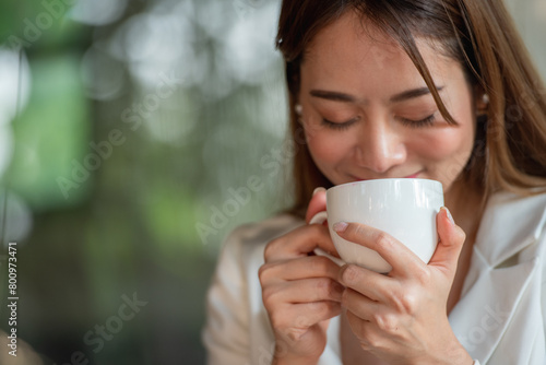 Asian woman holding hot coffee in paper mug cup to sniff smell of espresso in morning sunlight. girl carry coffee break to sniff fragrant smell the aroma of coffee.