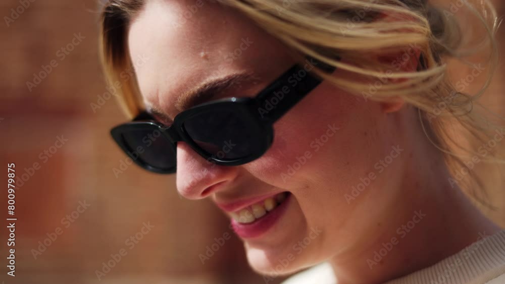 Close up view of attractive female face in sunglasses changing emotion from serious to happy on sunny day. Blond caucasian woman with beautiful smile and straight teeth enjoying spending time outside. Close up view of attractive female face in sunglasses changing emotion from serious to happy on sunny day. Blond caucasian woman with beautiful smile and straight teeth enjoying spending time outside.
