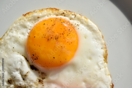 Close up fried egg on plate. Macro egg yolk sprinkled with black pepper photo
