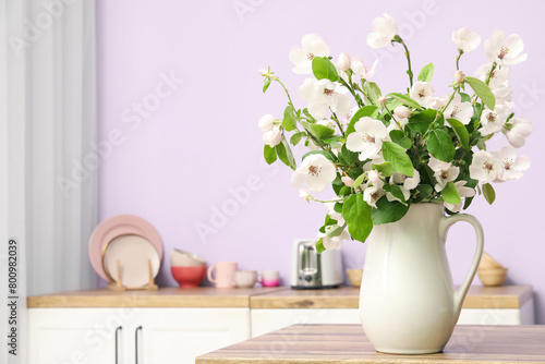 Vase with blossoming branches on table in kitchen