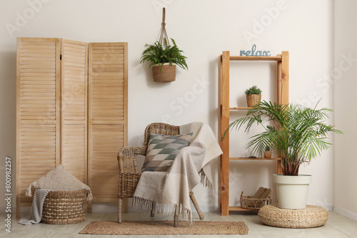 Stylish interior of living room with wicker armchair, plaid, pillow and houseplant