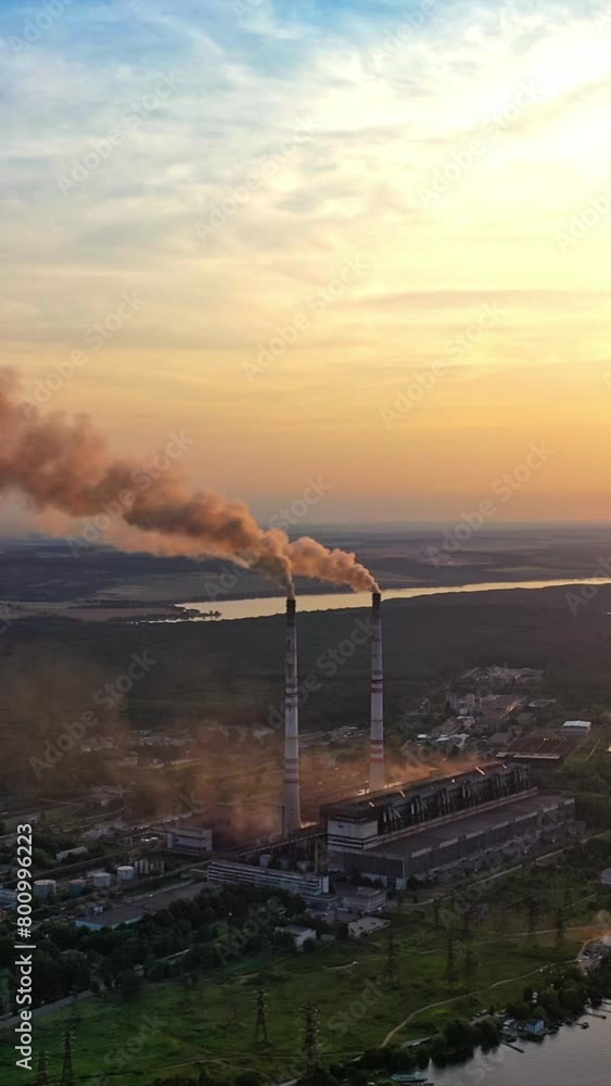 Smoke from pipes on factory near the river at sunset. Air pollution from industrial plant on the natural background in the evening. Vertical video Smoke from pipes on factory near the river at sunset. Air pollution from industrial plant on the natural background in the evening. Vertical video
