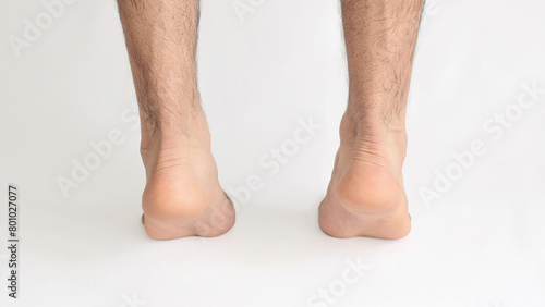Male feet standing on tiptoe viewed from behind at the Achilles heel, with white background and space for text