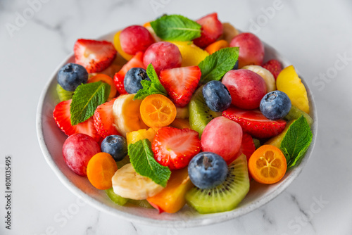 Summer fruit salad in a bowl on white marble background. Healthy diet food for breakfast. Mixed fruits  berries and mint for diet lunch