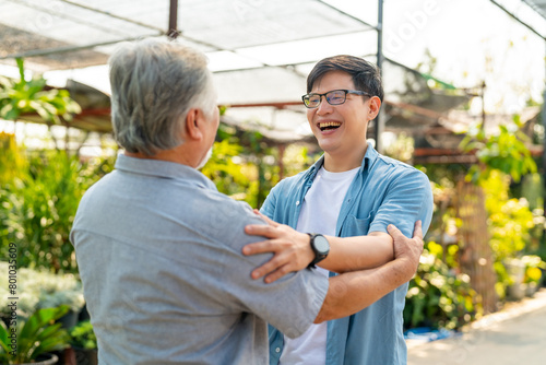 Happy Asian family spending time together on summer vacation. Adult son hugging elderly father during meeting and shopping together at plant shop street market. Family relationship concept.