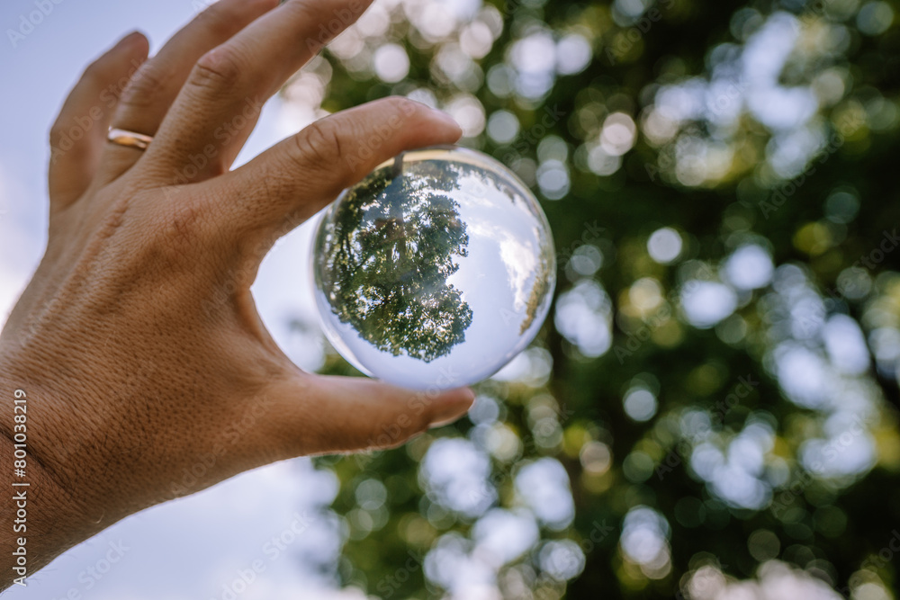 Valmiera, Latvia - August 19, 2023 - A hand holds a crystal ball which reflects an inverted image of trees against a bokeh background.