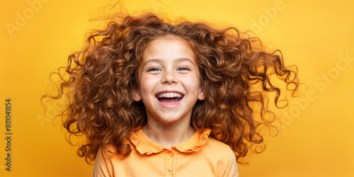 Cute young child  Little girl smiles. Emotion and child development. Little girl smiles while red hair.  A young girl with curly hair is smiling and laughing while wearing a shirt.