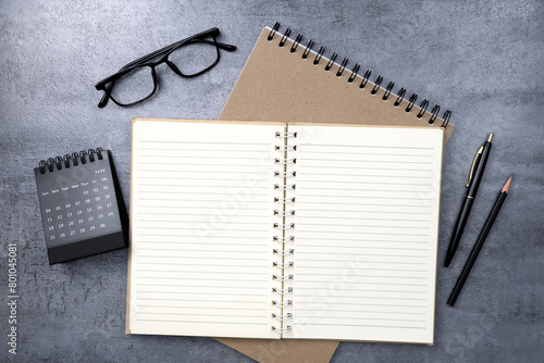 Notebook and black calendar and glasses on stone texture background. Work desk space