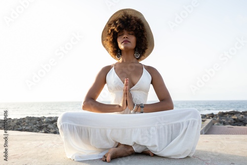 beautiful african woman with hat in yoga position with sunset background.