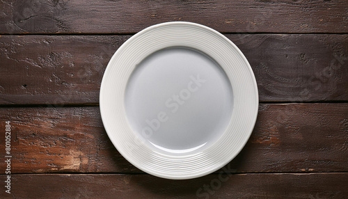 Empty round white plate on dark wooden table. Wood surface. Ceramic tableware. Top view