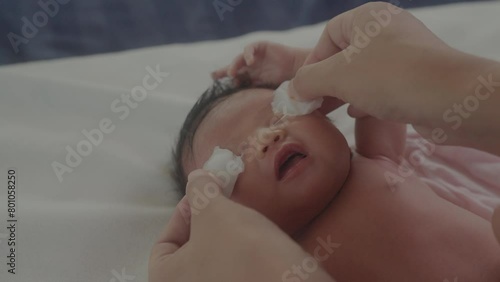 Closeup of mother wiping clean eyes of her newborn baby with wet cotton in slow motion