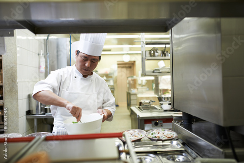 Chef, cooking and Asian man in restaurant with bowl mixing ingredients for meal, dinner or lunch. Catering, career and male culinary worker preparing Chinese cuisine or food in fine dining diner.