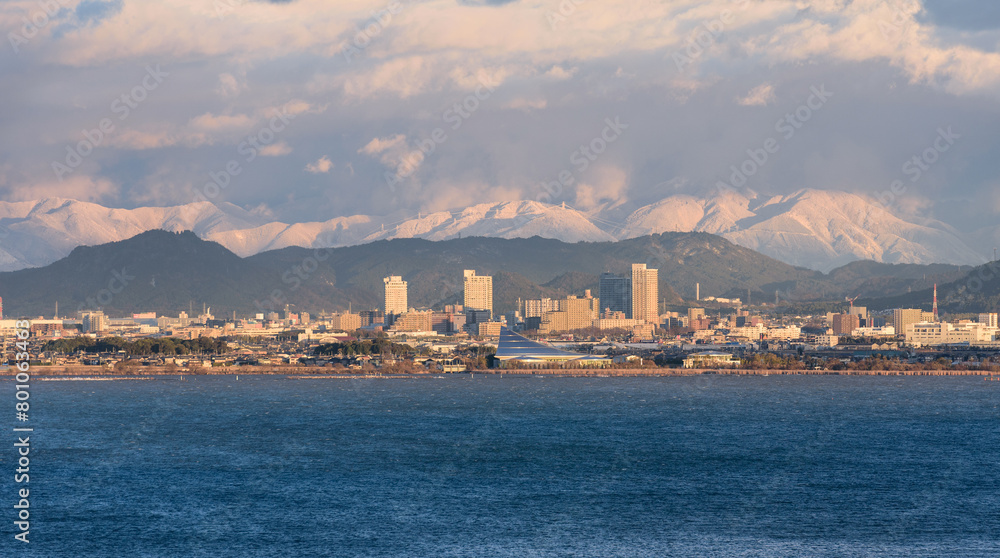 A view over Lake Biwa towards Kusatsu with snowy mountains in the background in Shiga Prefecture, Japan.
