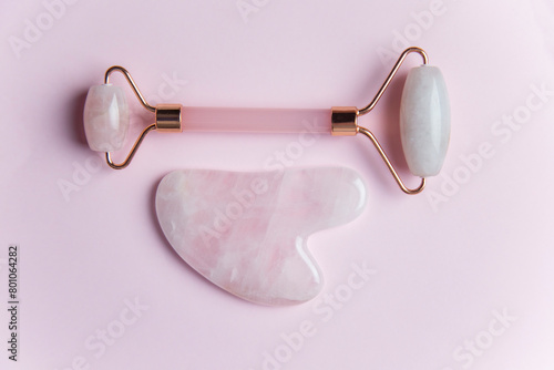 Facial massage roller and gua sha stone on pink background isolated copy space