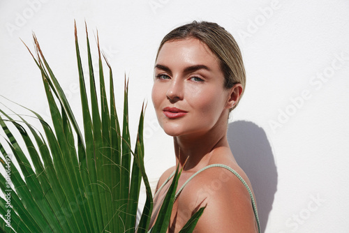 Portrait of Beautiful Young Woman Posing with Palm Leaf on White Background