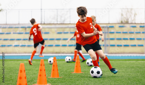 Happy Kids on Training Soccer Drill. Football Summer Camp. Young European Footballers Dribbling Around Cones in Drill. Soccer Boys in Red Uniforms in Training With School Young Coach