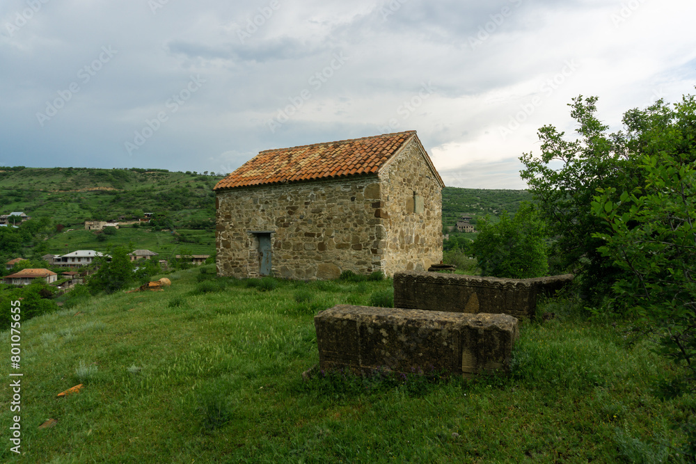 Obraz premium Gravestones in the courtyard of Church of Saskhori village, Georgia. Orange tile roof, Stone walls.