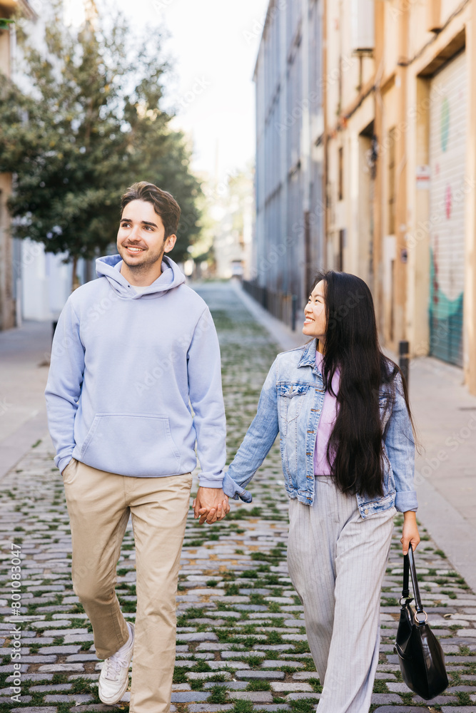 Interracial couple walking on a sidewalk holding hands. Young man and woman walking on city street.