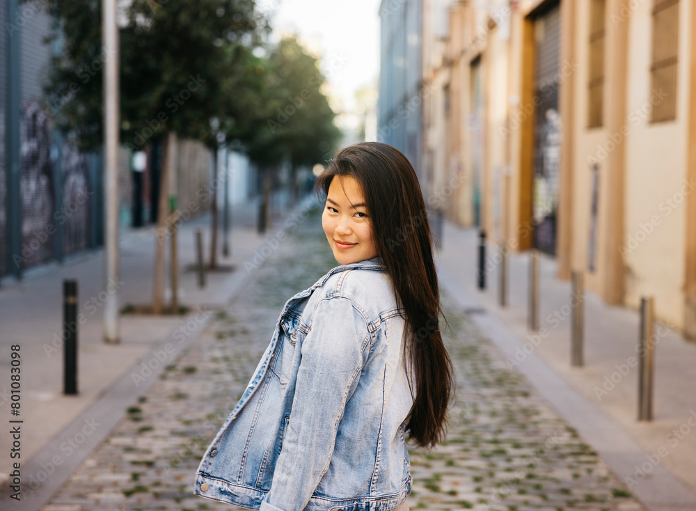 Portrait of a young beautiful smiling asian woman standing on sidewalk of a city street.
