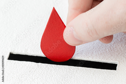 Red drop of blood symbol is put by person's hand into slot of white donation box. Concept of donorship, life-saving or health. Close-up shot