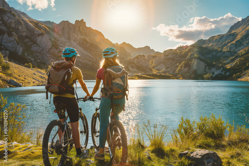 Young couple mountain biking looking at a bright blue mountain lake. The lake could be in the Alps, for example in Austria or Switzerland (A.I.-generated) photo