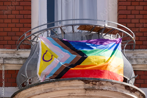 rainbow pride flag progress on balcony house, with black, brown, and blue lines trans flag in chevron form. Created by Daniel Quasar, international LGBT movement, Pride Month