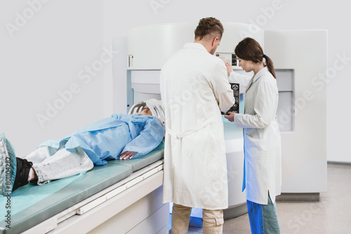 two doctors and a patient in the MRI room. Male doctor and female assistant preparing adult female patient for MRI scan