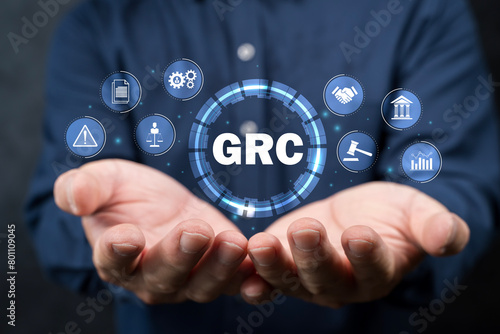 GRC, Governance Risk and Compliance concept. Businessman holding GRC icon on digital screen.