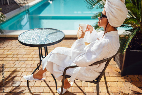 Relaxed caucasian female in sunglasses and a towel on her head sits at the poolside. © Dasha Petrenko