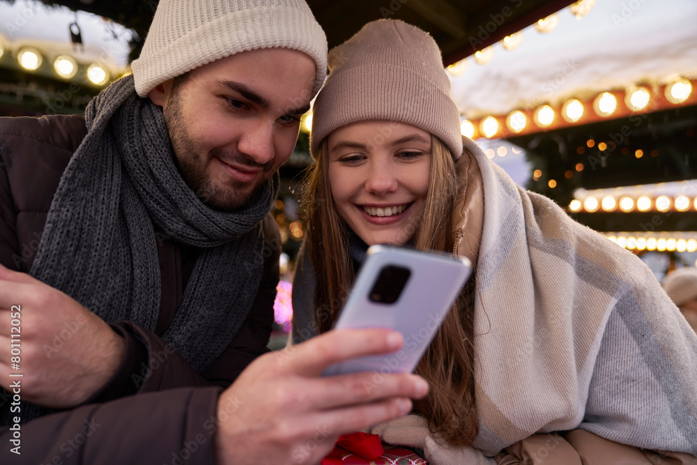 Fototapeta premium Young couple browsing phone together on Christmas Market at night