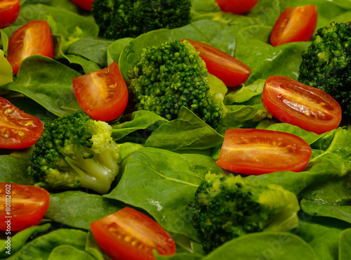 Pieces of broccoli cabbage, halved cherry tomatoes lie on fresh spinach leaves, background
