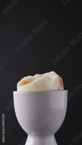 Boiled egg in an eggcup on a black background. It is taken with a spoon. Close-up of food photo