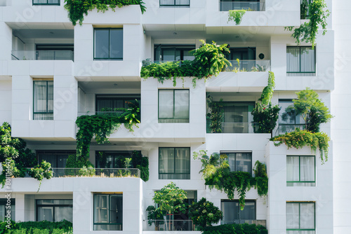Facade of a white modern apartment building with balconies covered in lush green plants