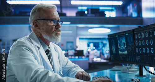 Senior Male Neuroscientist Using Desktop Computer To Analyze MRI Scans Of Brain In Medical Research Center Laboratory. Caucasian Doctor Studying CT Scan Of Stroke Patient's Brain, Finding Solutions.
