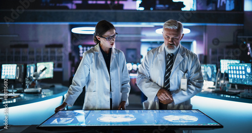 Modern Hospital Medical Research Center: Caucasian Female Neuroscientist And Male Surgeon Talking, Using Interactive Touch Screen Table With CT Scan Of Brain Damage Patient, Developing Solutions. © Gorodenkoff