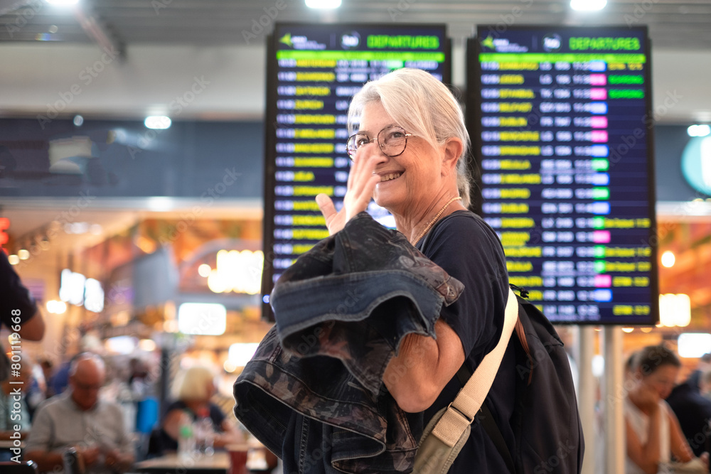 Woman traveler - senior lady standing inside airport terminal looking at timetable schedule. Travel and transportation themed image.