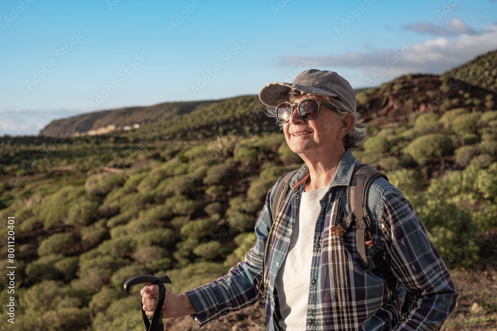 Portrait of carefree active caucasian senior woman with backpack and cap enjoying trekking day in countryside admiring landscape, Healthy lifestyle in retirement concept Portrait of carefree active caucasian senior woman with backpack and cap enjoying trekking day in countryside admiring landscape, Healthy lifestyle in retirement concept