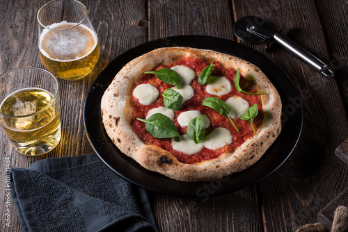 Pizza Margherita with basil and two glasses of beer on a black plate. Side view