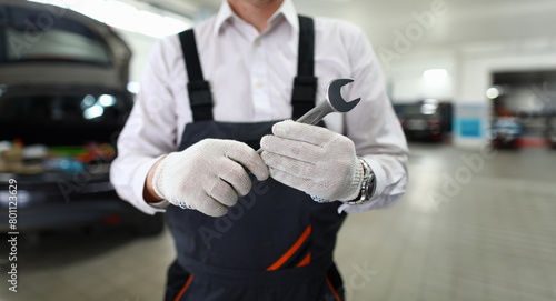 Focus on automechanic male hand in white gloves holding and showing utility for fixing car at camera. Machinery checkup and service station concept. Blurred background