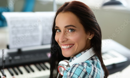 Close-up of smiling wonderful woman playing synthesizer on notes. Beautiful girl wearing fashionable smart earphones. Art music concept. Blurred background photo