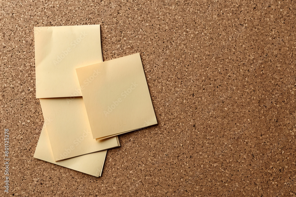 Three stacked yellow sticky notes on a textured cork background