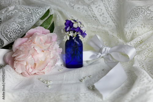 Pink peony and blue and white violets in an antique blue bottle. Ribbons, lace and pearls background.