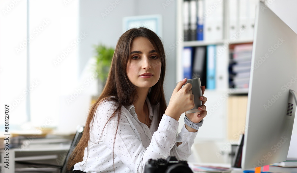 Pretty adult female sitting at worktable drinking hot beverage and looking in camera headshot Pretty adult female sitting at worktable drinking hot beverage and looking in camera headshot