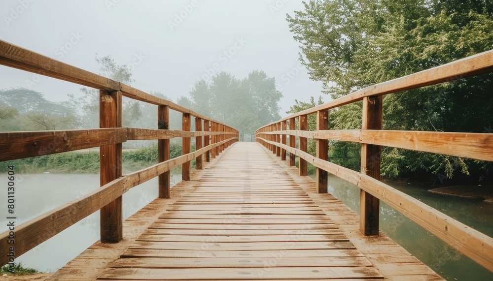 Tranquil morning mist envelops wooden bridge over serene lake surrounded by lush green trees