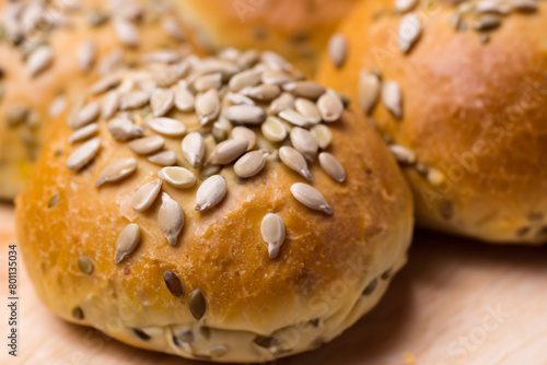 buns with seeds. on a wooden table lies a large number of small round fluffy buns sprinkled with sunflower seeds, close-up top view, concept of bakery products