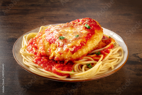 Chicken Parmesan, Italian pasta dish. Breaded chicken breast with cheese and spaghetti with tomato sauce, on a dark rustic wooden background