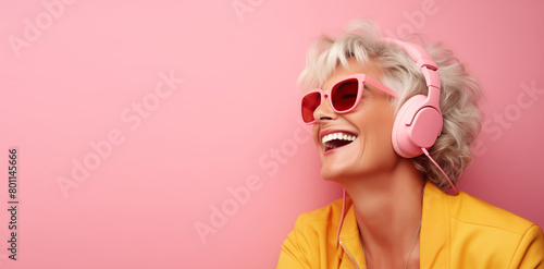 Portrait of happy laughing modern mature woman listening to music with headphones on pink background